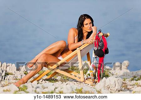 Attractive young woman in bikini lying on a beach chair with a bunch of swimsuits drying View Large Photo Image Stock Image - Attractive young woman in bikini lying on a beach chair with a bunch of swimsuits drying. Fotosearch