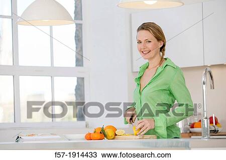 Stock Image - Attractive young woman in her kitchen cutting citrus fruits. Fotosearch
