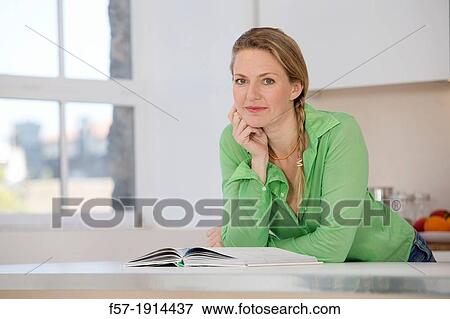 Attractive young woman in her kitchen reading a cookbook View Large Photo Image Stock Photo - Attractive young woman in her kitchen reading a cookbook. Fotosearch