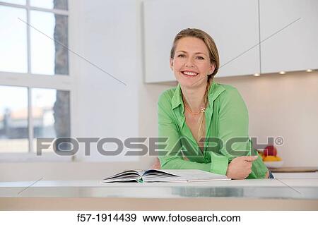 Attractive young woman in her kitchen reading a cookbook View Large Photo Image Stock Photo - Attractive young woman in her kitchen reading a cookbook. Fotosearch