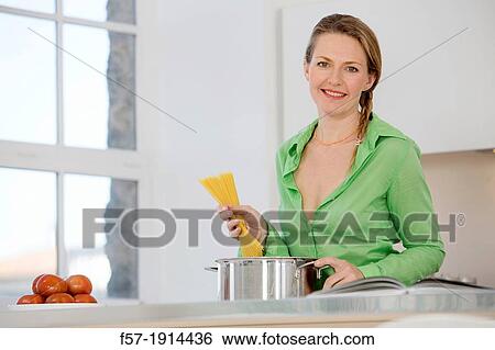 Stock Photograph - Attractive young woman in her kitchen cooking spaghetti. Fotosearch