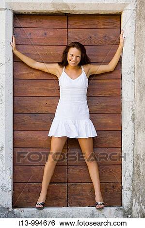 Stock Photograph - Attractive young woman in White short dress is standing on porch with spread hands and legs. Fotosearch