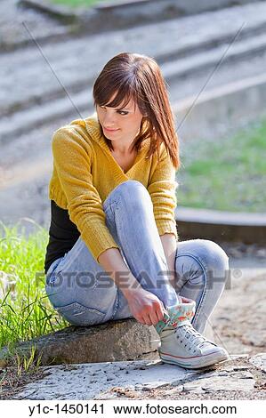 Stock Image - Attractive young woman is adjusting her sneakers in the park. Fotosearch