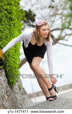 Stock Image - Attractive young woman is adjusting her sandals in the park. Fotosearch