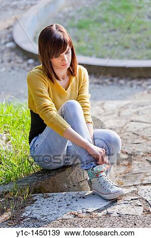 Stock Photo - Attractive young woman is adjusting her sneakers in the park. Fotosearch