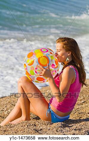 Attractive young woman is inflating a toy ball on the beach View Large Photo Image Stock Photo - Attractive young woman is inflating a toy ball on the beach. Fotosearch