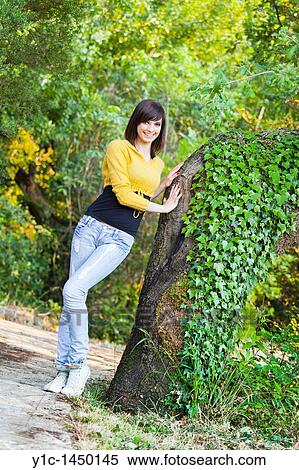 Stock Photography - Attractive young woman is posing happy by the big tree. Fotosearch