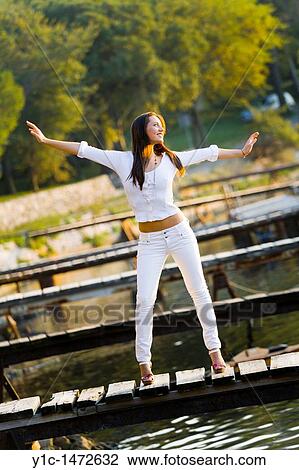 Stock Image - Attractive young woman is pretending to fly on a wooden pier. Fotosearch