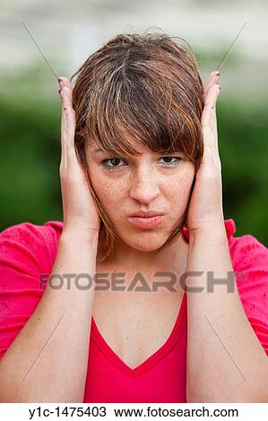 Stock Image - Attractive young woman is sad and cover her ears. Fotosearch