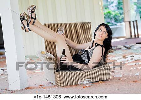 Stock Photograph - Attractive young woman is seated in a rotten chair, drunk. Fotosearch