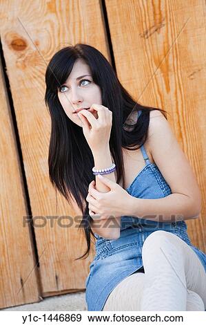 Stock Photo - Attractive young woman is sitting and thinking, biting fingernail. Fotosearch