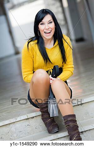 Stock Image - Attractive young woman is sitting in the street laughing. Fotosearch