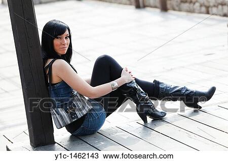 Stock Image - Attractive young woman is sitting on a wooden floor. Fotosearch