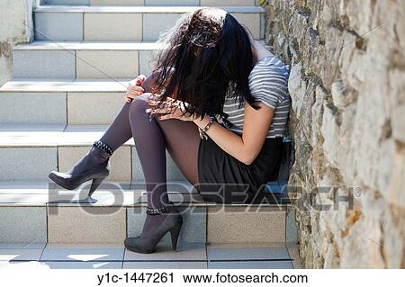 Stock Image - Attractive young woman is sitting on the staircase hiding identity. Fotosearch