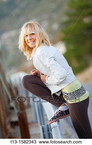 Attractive young woman is smiling with her leg high on a fence View Large Photo Image Stock Image - Attractive young woman is smiling with her leg high on a fence. Fotosearch