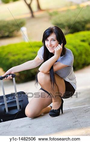 Attractive young woman is squatting next to a travel suitcase View Large Photo Image Stock Photograph - Attractive young woman is squatting next to a travel suitcase. Fotosearch
