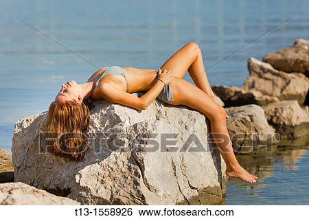 Attractive young woman is sunbathing in an awkward position on the rock View Large Photo Image Stock Photograph - Attractive young woman is sunbathing in an awkward position on the rock. Fotosearch