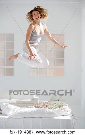 Attractive young woman jumping on her bed View Large Photo Image Stock Photo - Attractive young woman jumping on her bed. Fotosearch