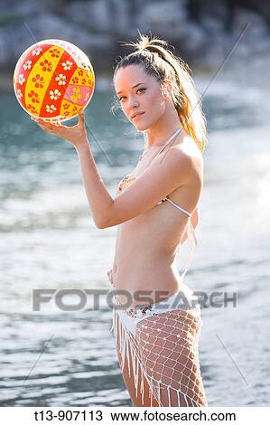 Stock Image - Attractive young woman on beach with colorful ball in hands. Fotosearch