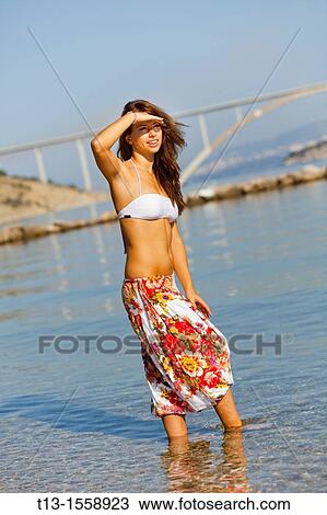 Stock Image - Attractive young woman on the beach before a bridge. Fotosearch