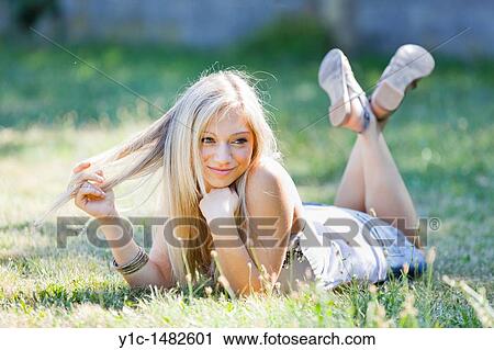 Stock Image - Attractive young woman portrait happy lying on the grass. Fotosearch