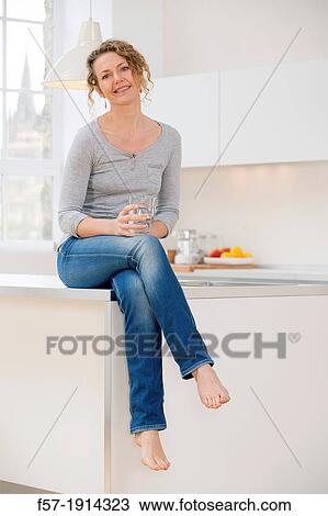 Attractive young woman sitting in her kitchen driking water View Large Photo Image Stock Image - Attractive young woman sitting in her kitchen driking water. Fotosearch