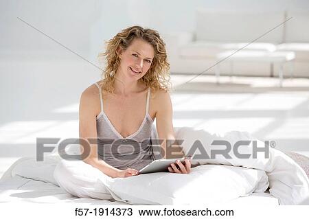 Attractive young woman using her tablet computer in bed View Large Photo Image Stock Image - Attractive young woman using her tablet computer in bed. Fotosearch