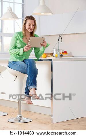 Attractive young woman using her tablet computer in her kitchen View Large Photo Image Stock Image - Attractive young woman using her tablet computer in her kitchen. Fotosearch