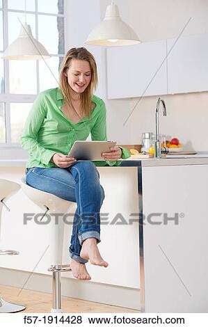 Stock Photo - Attractive young woman using her tablet computer in her kitchen. Fotosearch