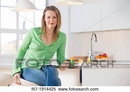 Stock Photography - Attractive young woman using her tablet computer in her kitchen. Fotosearch