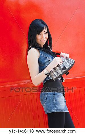 Stock Photo - Attractive young woman with a purse before a bright Red wall. Fotosearch