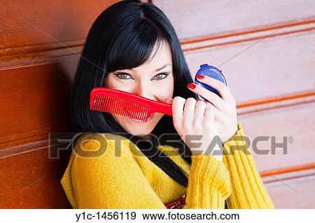 Stock Photo - Attractive young woman with a Red brush in hand, hiding face. Fotosearch