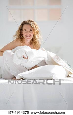 Stock Photography - Attractive young woman wrapped in her quilt in bed. Fotosearch