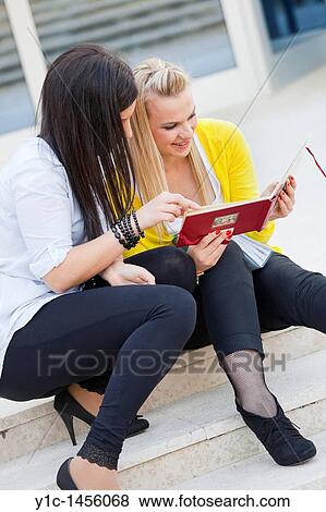 Stock Photo - Attractive young women are sitting on low steps and looking at album photos. Fotosearch