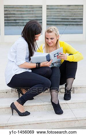 Attractive young women are sitting on low steps and looking at album photos View Large Photo Image Stock Photo - Attractive young women are sitting on low steps and looking at album photos. Fotosearch