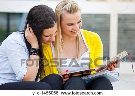Stock Photograph - Attractive young women are sitting on low steps and looking at album photos. Fotosearch