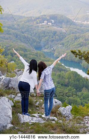Stock Photograph - Attractive young women pretend to fly looking down the mountain. Fotosearch