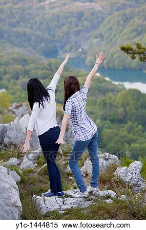 Stock Photography - Attractive young women pretend to fly looking down the mountain. Fotosearch