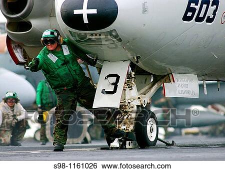 Stock Photograph - Aviation Boatswain's Mate 3rd Class Robert Lightner signals to have the catapult shuttle moved forward in order to place an E-2C Hawkeye. Fotosearch