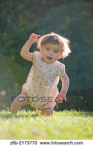 Stock Image - Baby, 10 Months Old, Outdoors, Sunlight, waving, rising, Effort, Challenge, Balance, Garden. Fotosearch