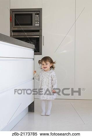 Stock Photography - Baby girl, 17/18 Months, Kitchen, Oven, Microwave, White goods, Tooth, Toothless, Woollen Tights, Pigtails, Barefoot. Fotosearch