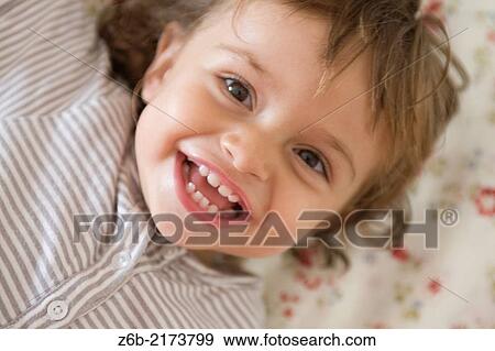 Stock Photo - Baby girl, 23 months, Toddler, Overhead shot, teeth, toothless, button, flowered, bed linen. Fotosearch