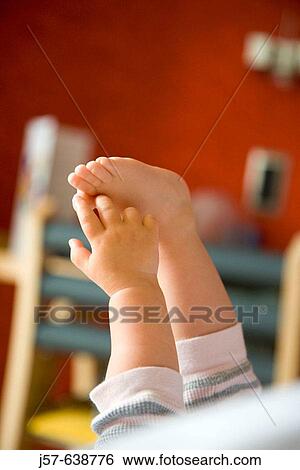 Stock Photograph - Baby girl playing with feet on bed in hotel.. Fotosearch