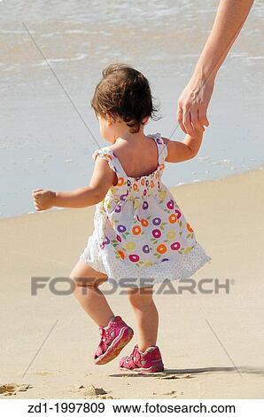 Stock Photo - Baby girl wearing her first shoes walking on the beach with here mother.. Fotosearch