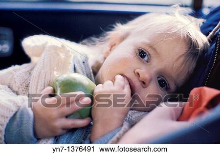 baby lying in the back seat of a car holding a green apple lost in thought View Large Photo Image Stock Image - baby lying in the back seat of a car holding a green apple lost in thought. Fotosearch
