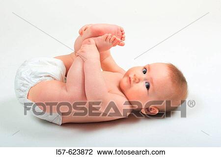 Stock Image - Baby lying on back, wearing nappies, playing with its feet, Studio, Oetwil am See, Zuerich, Switzerland. Fotosearch