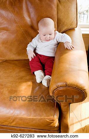Stock Image - Baby sitting on a leather couch. Fotosearch