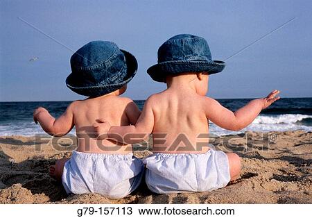 Stock Image - Baby twin sisters sitting on the beach. Fotosearch