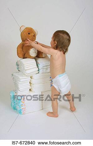 Baby wearing nappies, standing and playing with teddy bear and nappies, pile of nappies View Large Photo Image Stock Image - Baby wearing nappies, standing and playing with teddy bear and nappies, pile of nappies. Fotosearch