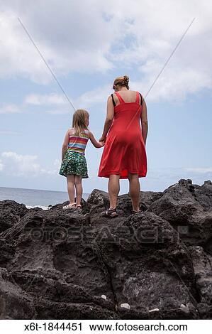 back of mother wearing a red dress, holding hands with a young girl in a striped shirt and a flower printed skirt both are standing on giant lava rocks looking out into the ocean. View Large Photo Image Stock Image - back of mother wearing a red dress, holding hands with a young girl in a striped shirt and a flower printed skirt both are standing on giant lava rocks looking out into the ocean.. Fotosearch